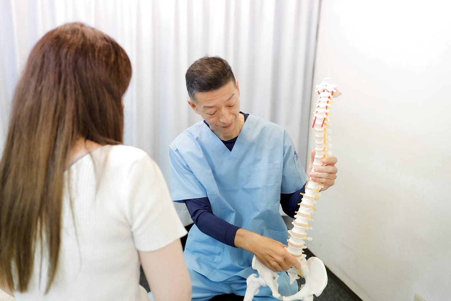 骨盤と腰椎の模型を指しながら、腰の状態を説明する清水接骨院の院長